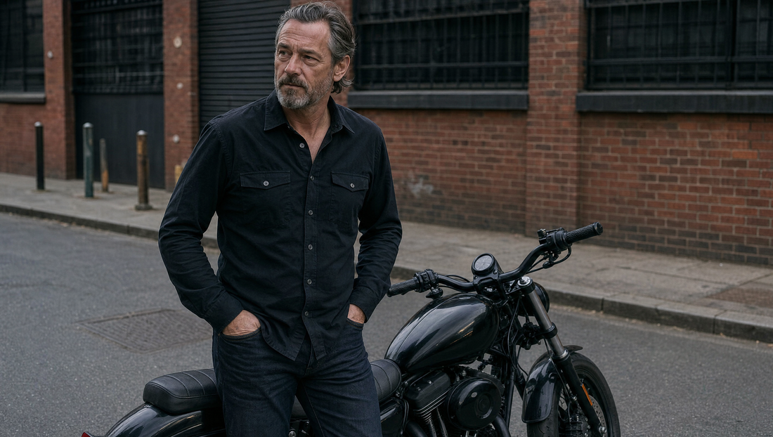 Motorcycle rider in dark casual armored streetwear leaning on a blacked-out cruiser on a city street