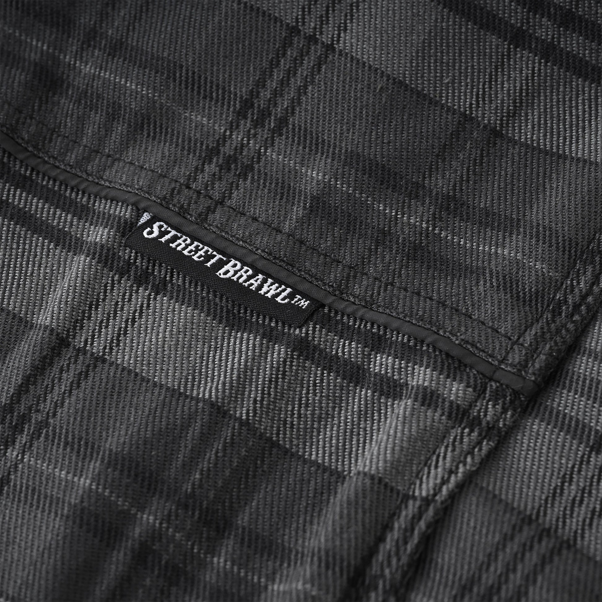 Close-up of a dark gray and black plaid fabric with a visible black label reading STREET BRAWL™.