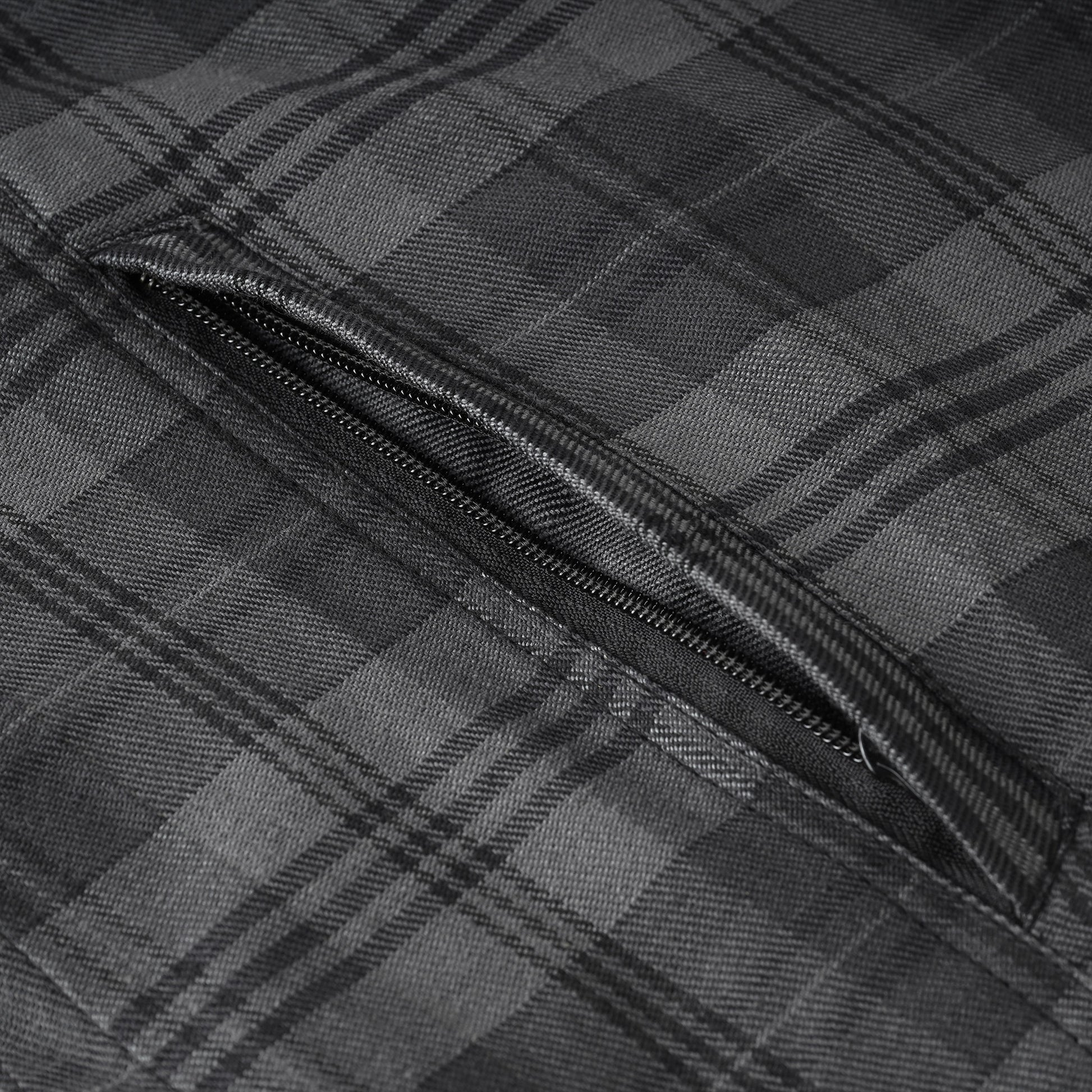 Close-up of a dark gray and black plaid fabric with a diagonal zippered pocket.