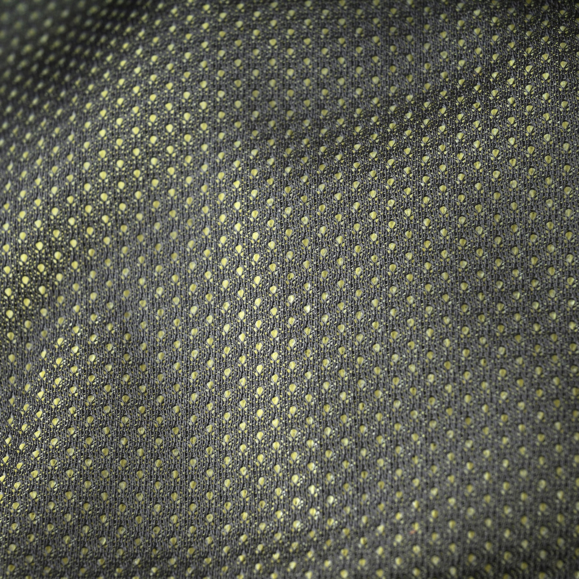 A close-up of a woven fabric with a repeating small geometric dot pattern in muted yellow-green on a dark charcoal gray background.