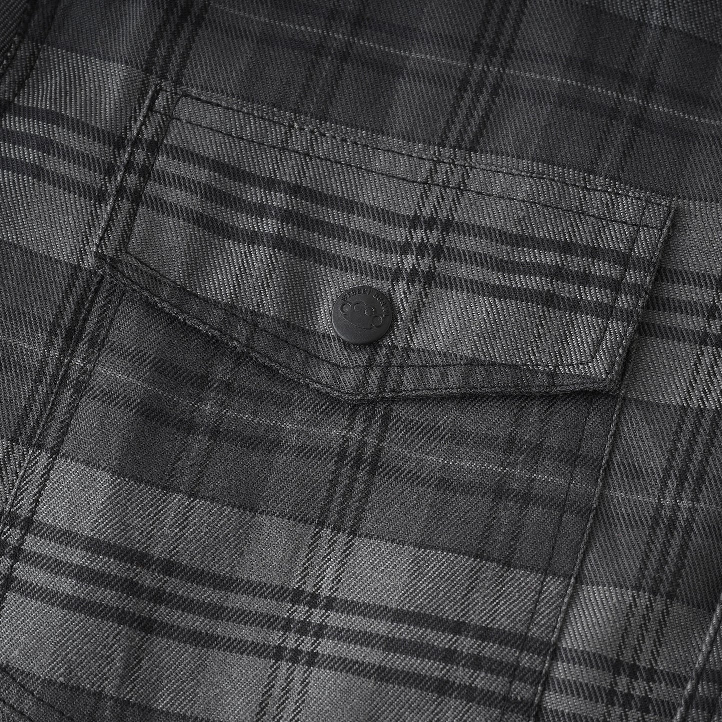 Close-up of a dark gray and black plaid fabric with a buttoned chest pocket.