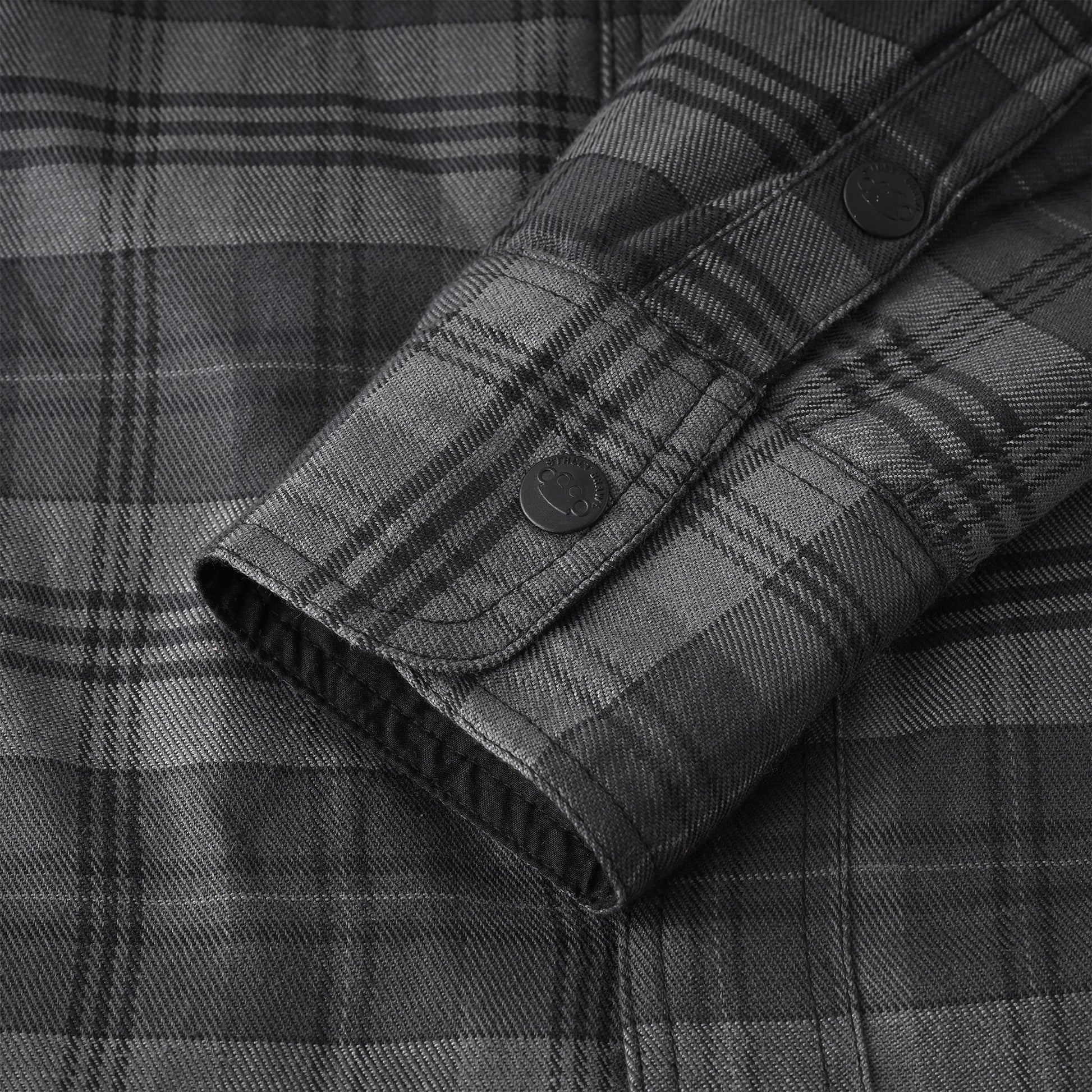 Close-up of a dark gray and black plaid button-down shirt showing the fabric texture and cuff detail.