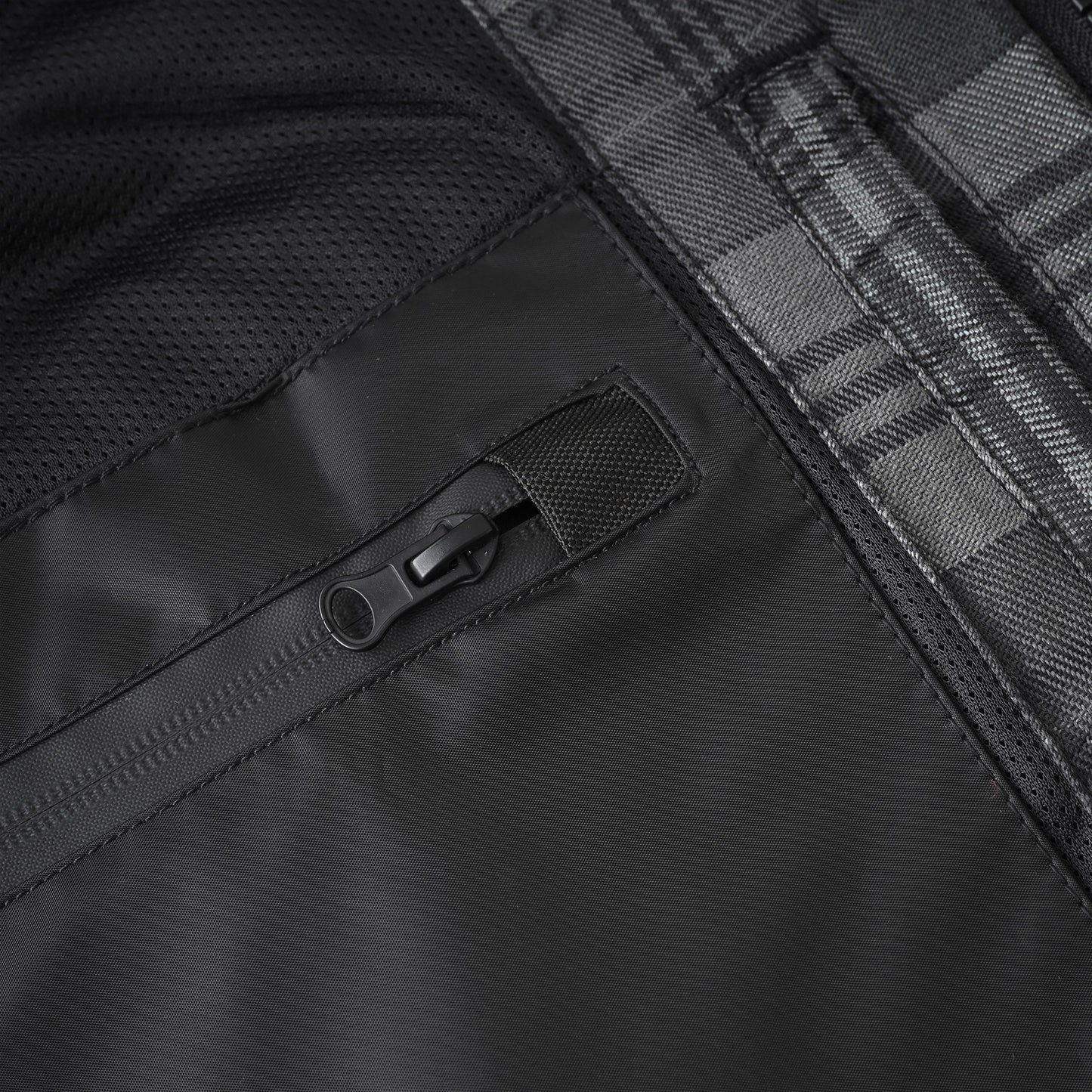 Close-up detail of a black waterproof jacket showing a black zipper pocket, black mesh fabric, and a gray and black plaid pattern.